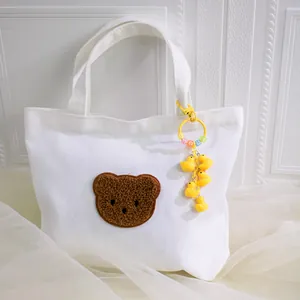 Cute yellow duck beaded keychain hanging on a white canvas tote bag with a brown teddy bear