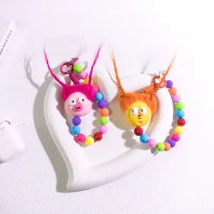 Close-up of colorful beaded phone straps with fuzzy cartoon charms in a ceramic dish