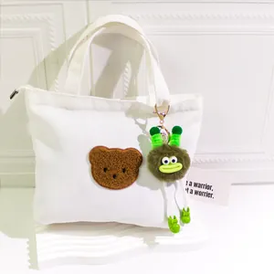 White canvas tote bag with brown teddy bear patch and green fuzzy monster keychain charm