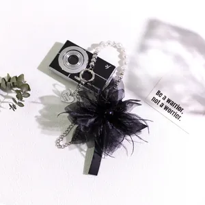 Close-up of black fabric flower keychain with pearls and heart charm on metal chain
