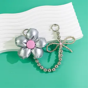 Detail of silver metallic flower keychain with pink center and beaded bow charm