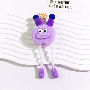 Close-up of a purple monster plush keychain with big eyes and rope legs on a stylish base