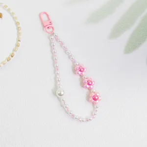 Close-up of pink floral keychain with pearl beads and shadow on white background