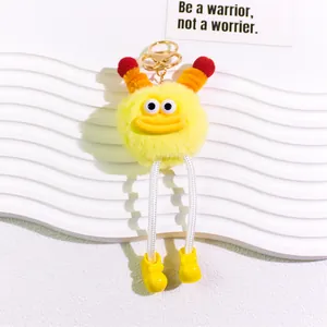 Detail of yellow plush monster keychain with big eyes and orange tentacles on a white stand