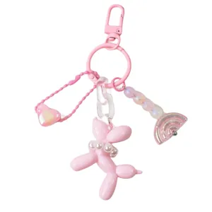Pink resin balloon dog keychain with pearl necklace and rainbow charm on white background