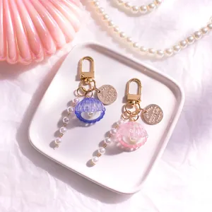 Dettaglio di portachiavi a conchiglia rosa e blu con perle su un vassoio bianco