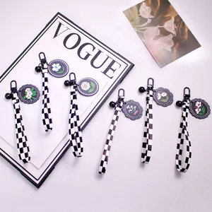 Checkered leather ribbon keychain with daisy acrylic pendants and black bells on pink background