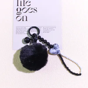 Close-up of DIY keychain with black faux fur pompom, marble heart and beaded chain detail