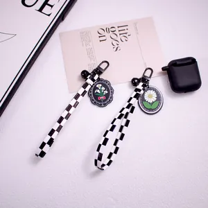 Detail of checkerboard strap keychain with daisy charm and black carabiner on desktop
