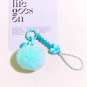 Detail of mint green plush ball keychain with marble heart bead and blue bell charm