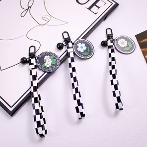 Close-up of black and white checkered ribbon keychain with daisy floral charms and bell