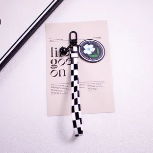 Close-up of checkerboard lanyard keychain with black bell and white daisy floral charm