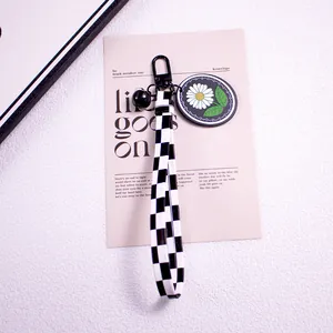 Detail of checkered ribbon keychain with daisy pendant and matte black metal hardware