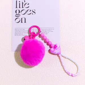 Detail of rose red faux fur pompom keychain with heart beads and a small bell