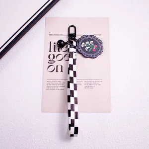 Close-up of checkered ribbon keychain with black daisy charm and matte metal clip