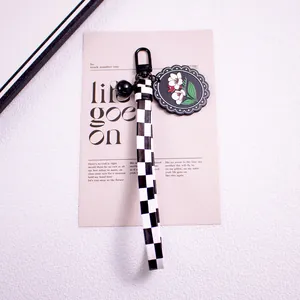 Detail of checkerboard strap keychain with black bell and floral acrylic charm