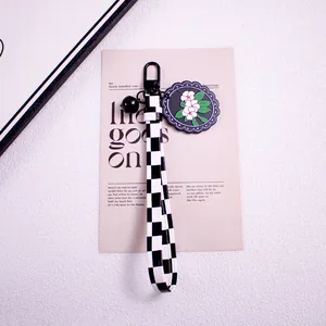 Detail of checkered wrist strap keychain with daisy floral pendant and black bell charm