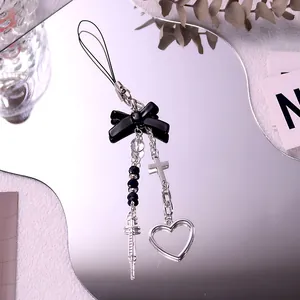 Detail of gothic Y2K phone charm with black bow, silver syringe and cross on mirror