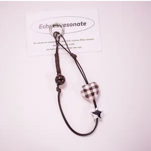 Detail of plaid heart and silver star charms on a brown woven rope phone lanyard strap