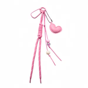 Porte-clés cœur en cuir rose avec corde tressée et perles décoratives sur fond blanc