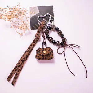 Detail of leopard print mini bag charm with heart clasp, beads and brown bow accent