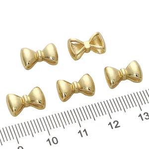 Cinque ciondoli a fiocco in oro 14K per gioielli fai-da-te mostrati su un righello graduato