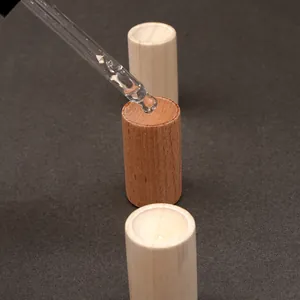 Detalle de un gotero de vidrio aplicando aceite en difusores de madera cilíndricos
