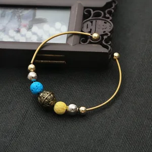1.8mm golden open bangle with blue and yellow lava stones and metal charms on dark fabric