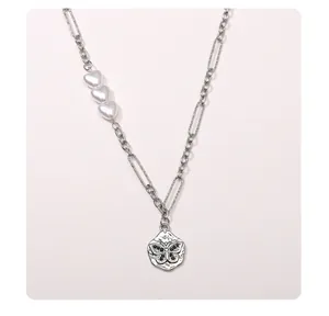 Détail du collier à maillons asymétriques avec perles en cœur et pendentif papillon