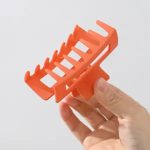 Große matte orangefarbene Haarklammer in der Hand gehalten vor grauem Hintergrund