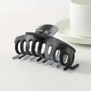 Detail of a large matte charcoal shark hair claw clip with golden metal spring on a table