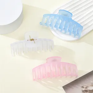 Three large matte hair claws in light blue, white, and pink on minimalist display pedestals