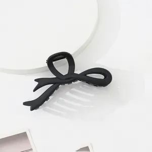 Detailed close-up of matte black bow hair claw clip on a minimalist white display
