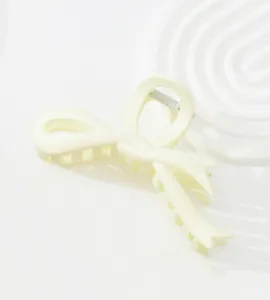 Detail of off-white bow hair claw clip with matte finish on decorative wave plate