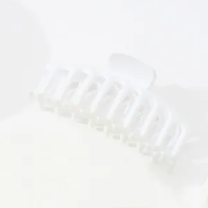 Détail d'une grande pince à cheveux blanc mat avec un design incurvé à dents multiples