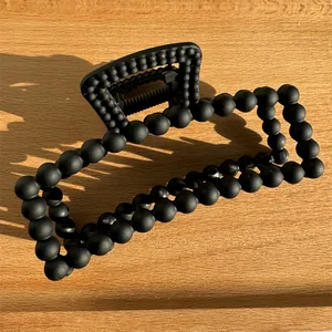 Close-up of black matte bead hair claw clip on a wooden surface with metal spring detail