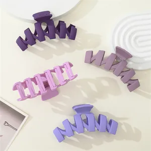 Detail of four matte purple hair claw clips with wavy geometric design on stone props