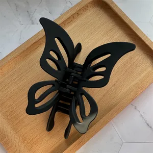 Close-up of matte black hollow butterfly hair claw clip on a wooden display tray