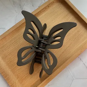 Matte brown butterfly hair claw clip with cutout design on a wooden tray