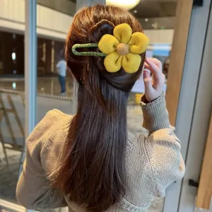 Details einer gelben Plüsch-Blumen-Haarspange mit grünem Clip an dunklem Haar