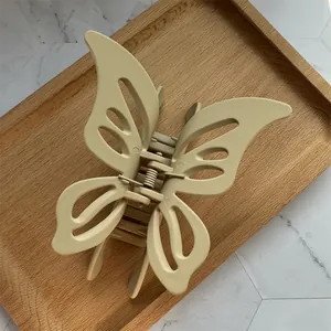 Detail of a matte beige butterfly hair claw clip with a hollow design on a wooden tray