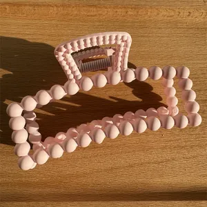 Detail of matte pink rectangular hair claw clip with ball bead texture on light wood