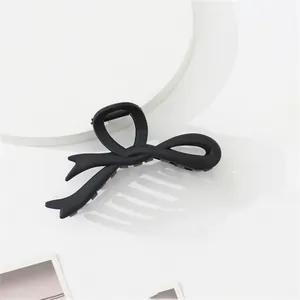 Detail of matte black resin hair claw clip with bow design on a minimalist white stand