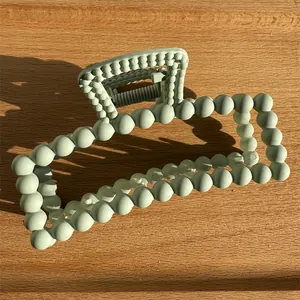 Close-up of mint green matte rectangle hair claw clip with round bead design on wood