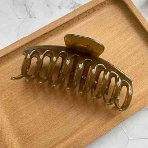 Detail of large translucent olive green hair claw clip on a modern wooden tray
