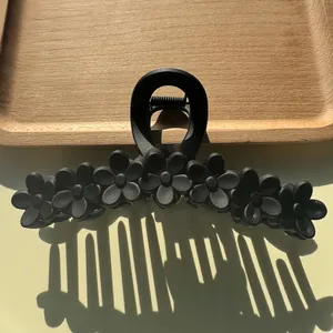 Détail de pince à cheveux fleur noire mate sur plateau en bois avec ombre de lumière naturelle