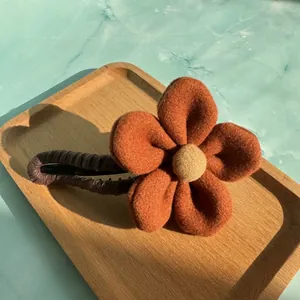 Detailansicht der flauschigen orangefarbenen Blumen-Haarklammer auf einem Holztablett