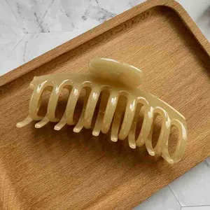 Detail view of large cream jelly hair claw clip on wooden tray with marble background