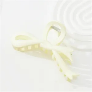 Detail of matte cream bow hair claw clip with metallic spring on a textured tray