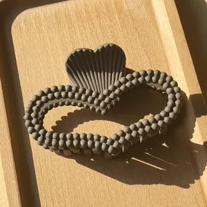 Top view of large matte dark grey heart-shaped claw clip with bead texture on a wooden tray